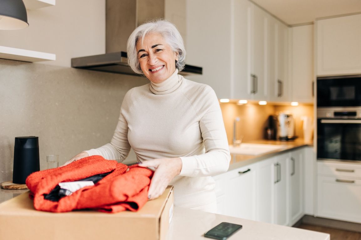 Senior woman smiling while unpacking clean folded laundry showing example of Nashville laundry delivery for seniors in her kitchen