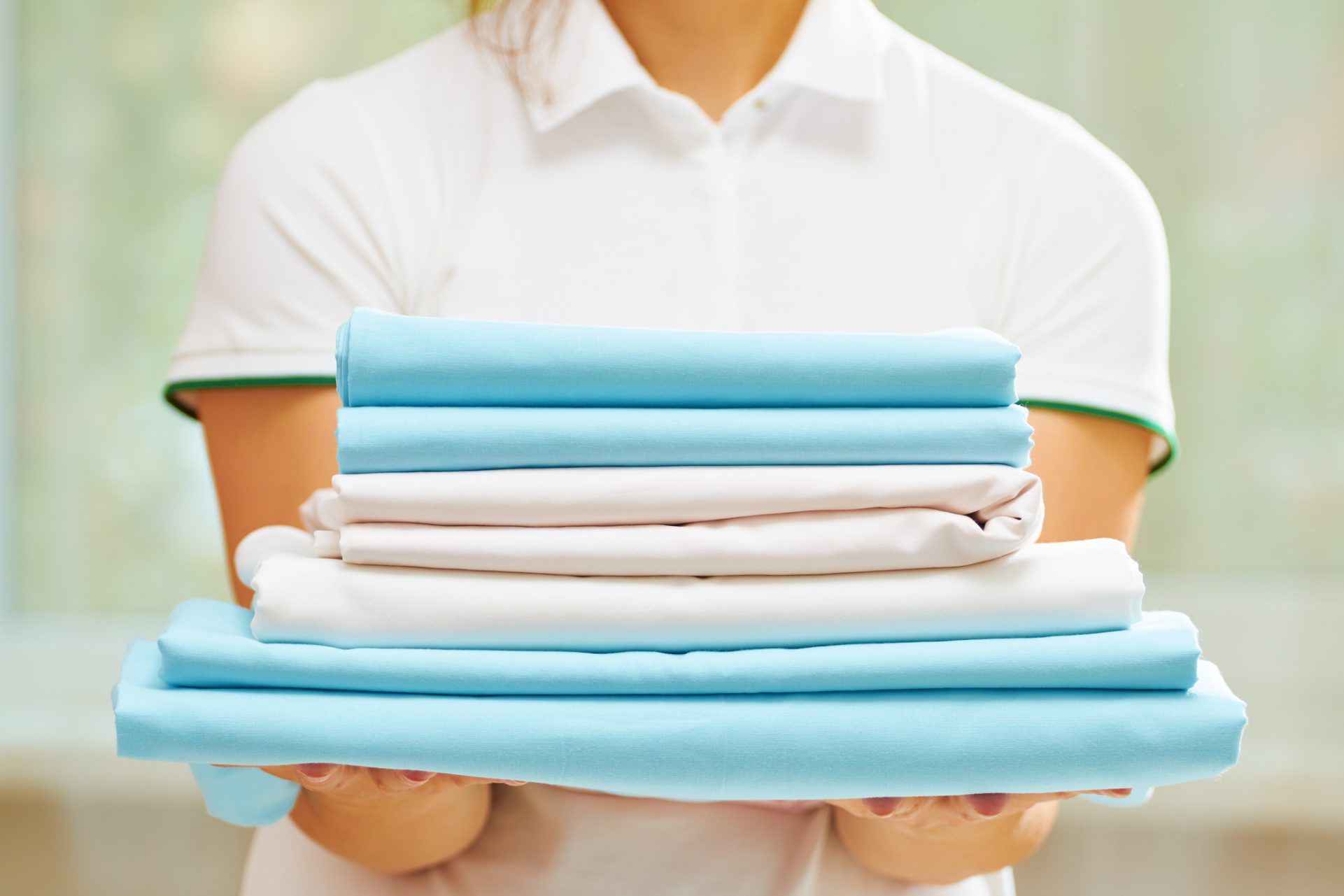 Closeup of woman's hand holding a stack of clean folded linens of blue and white colors.