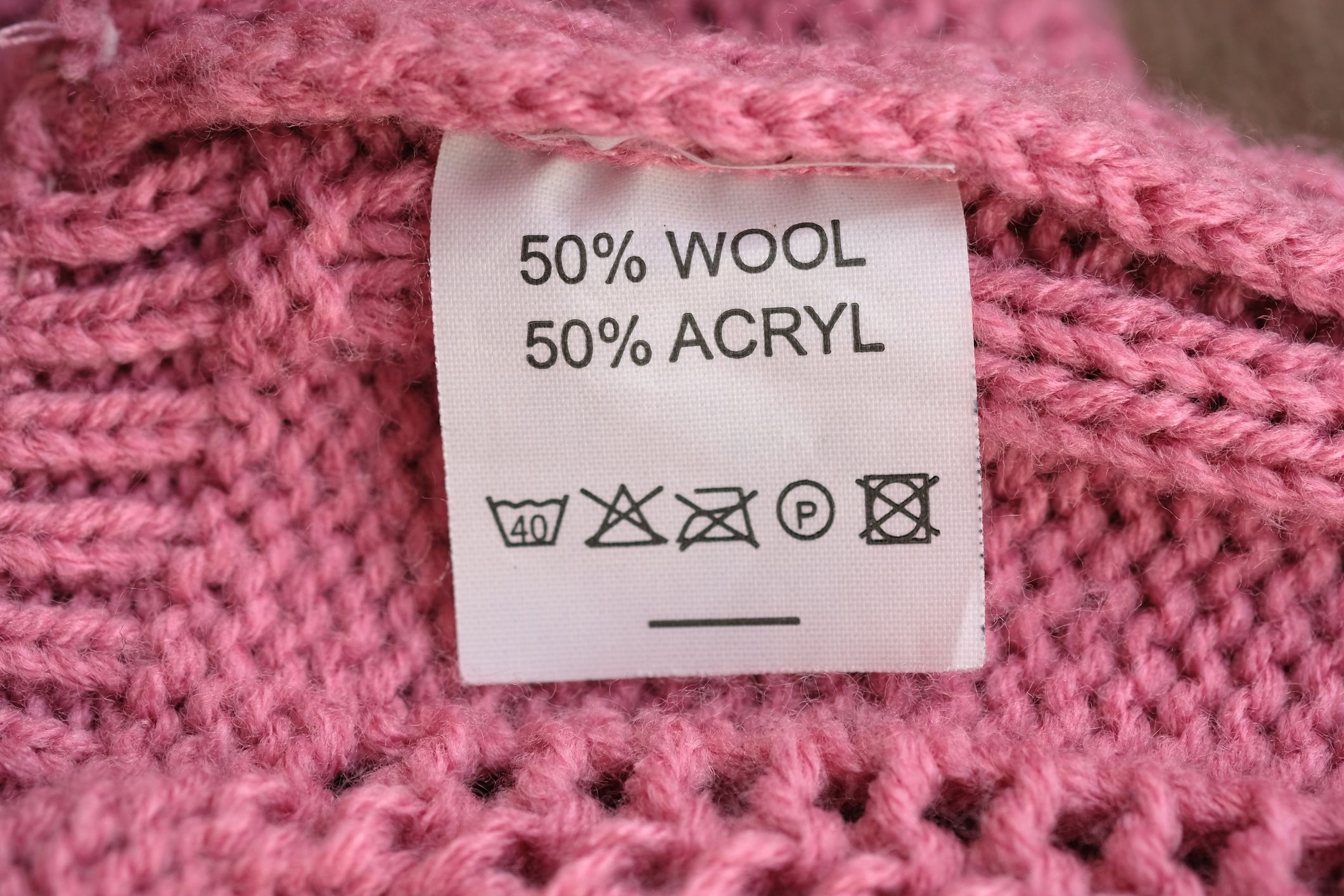 Wrong side of a pink knitted sweater made of wool, the composition is specified as well as care instructions