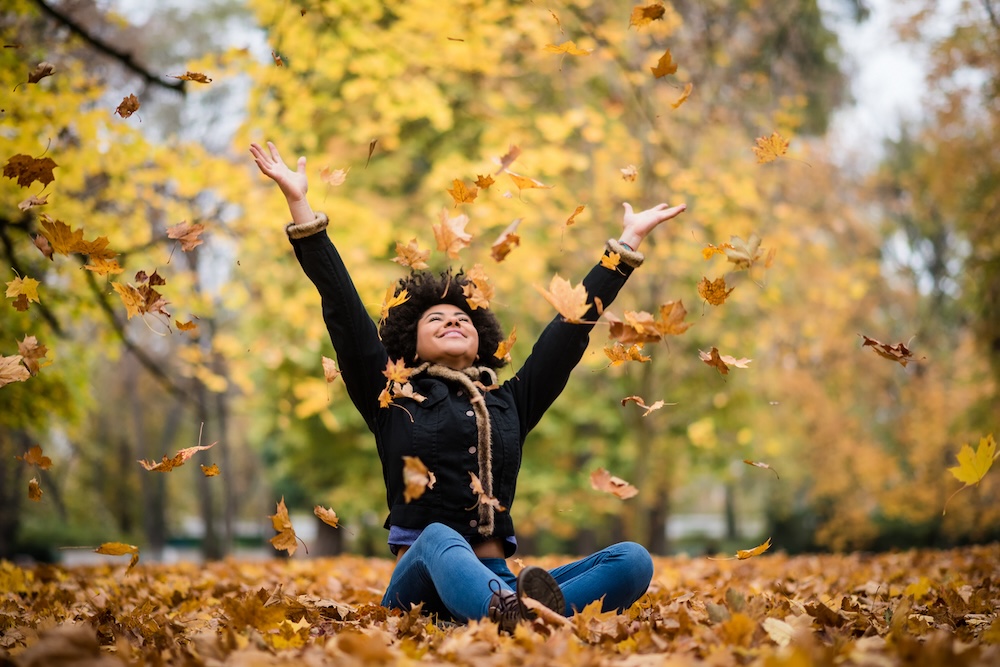 Woman playing with fall leaves in Nashville—enjoy a stress-free fall wardrobe transition with laundry pickup service.